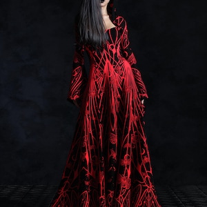 May include: A long, flowing black dress with a striking red pattern. The dress features a hood and flared sleeves. The intricate design covers the entire garment, creating a dramatic and gothic aesthetic. The dress is suitable for cosplay or themed events.