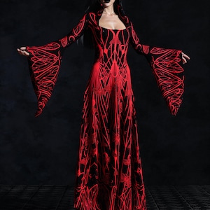 May include: A long, black dress with a red, intricate, floral-like pattern. The dress features long, flared sleeves and a square neckline. The design is symmetrical, with the red pattern standing out against the black fabric. The dress appears to be made of a flowing material.