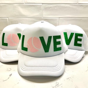 May include: Three white trucker hats with green glitter lettering that says "LOVE" with a pink tennis ball graphic.