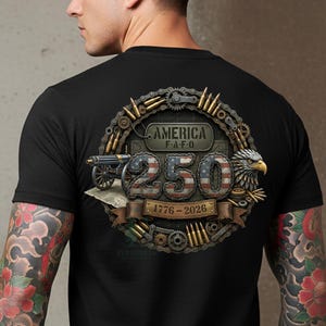 以下が含まれることがあります： 愛国的なデザインの黒いTシャツ。デザインには、アメリカ国旗のパターン、大砲、ワシとともに、数字「250」の上に「AMERICA」という言葉が含まれています。「1776-2026」というテキストも表示されています。