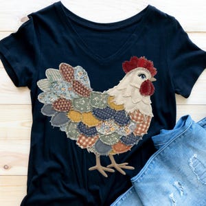 May include: A navy blue V-neck t-shirt with a patchwork rooster design. The rooster has a white body, red comb, and a tail made of various patterned fabric pieces in shades of blue, green, yellow, and brown. A pair of blue jeans is visible.
