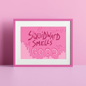 Könnte beinhalten: Rosa gerahmter Druck mit einem rosa und weißen Farbverlaufshintergrund. Der Text "Squidward Smells Good" ist in einer tropfenden rosa Schrift geschrieben.