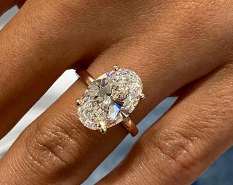 May include: A rose gold engagement ring featuring a large, oval-cut diamond. The diamond is set with four prongs and sparkles brightly. The ring is shown on a person's finger.