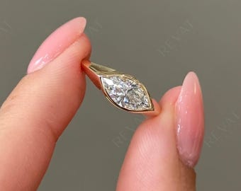 May include: A gold ring featuring a marquise-cut clear gemstone set in a smooth bezel setting. The band is solid gold and tapers slightly toward the center, where the elongated, pointed stone is securely held in a polished metal frame.