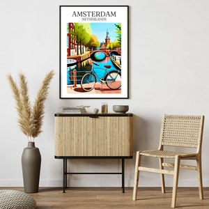 Op de afbeelding: Een kleurrijke illustratie van een fiets geparkeerd aan een kanaal in Amsterdam, Nederland. De afbeelding toont een blauw kanaal met een brug, gebouwen en bomen. De tekst "AMSTERDAM" en "NEDERLAND" staat bovenaan de afbeelding.