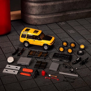 May include: A yellow and black toy SUV with a black roof, surrounded by disassembled parts, including wheels, a chassis, and tools. The toy car has a sunroof and is set against a dark, textured surface.