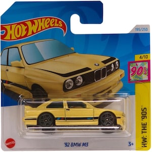 Puede incluir: Coche de juguete '92 BMW M3 amarillo de la serie Hot Wheels '90s. El coche tiene ruedas negras, una franja negra y detalles en azul y rojo. El embalaje incluye el logotipo de Hot Wheels, el número 195/250 y el texto "HW: THE '90S."
