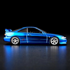 以下が含まれることがあります： 青いスポーツカー。Type Rのエンブレム、スポイラー、白いホイールが特徴です。黒い背景に配置され、下に反射面があります。クーペです。