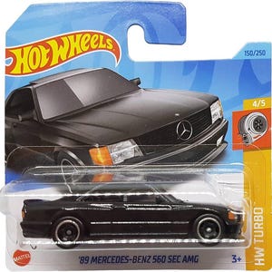 May include: A black 1989 Mercedes-Benz 560 SEC AMG Hot Wheels die-cast car with a black plastic base and a clear plastic window. The car has a black interior and a black exterior. The car is on a blue and white card with the words "Hot Wheels" and "HW TURBO" printed on it. The car is number 150/250 in the series.