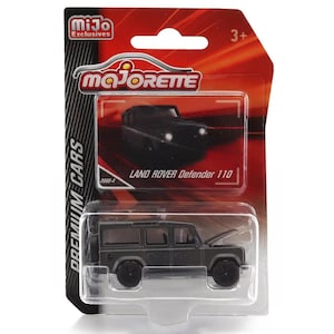 May include: A die-cast Land Rover Defender 110 toy car in a blister pack. The dark gray model has its hood open, revealing engine details. The packaging features the "Majorette" logo and the text "LAND ROVER Defender 110".