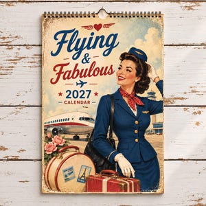 Puede incluir: Un calendario de pared 2027 titulado Flying & Fabulous con una ilustración de estilo vintage de un asistente de vuelo con uniforme azul y pañuelo rojo, junto a un avión, una maleta redonda con pegatinas de viaje y una maleta roja.