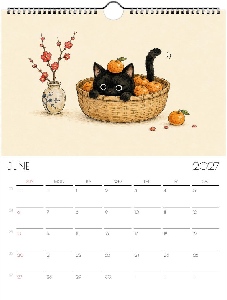 Puede incluir: Una p&aacute;gina de calendario de pared de junio de 2027 con una ilustraci&oacute;n de un gatito negro sentado en una cesta tejida llena de naranjas. Una peque&ntilde;a naranja descansa sobre la cabeza del gatito. Junto a la cesta hay un jarr&oacute;n con flores rojas.