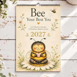 Puede incluir: Un calendario de pared 2027 titulado Bee Your Best You, A 12 Month Calendar of Kindness, Balance & Joy. La portada presenta una ilustración central de una abeja peluda sentada sobre una margarita blanca, sosteniendo un corazón rosa.