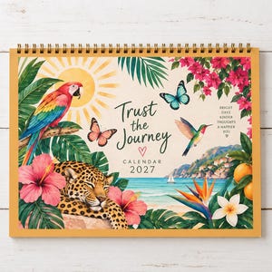 Könnte beinhalten: Ein Wandkalender für 2027 mit Spiralbindung, der eine tropische Szene mit einem Ara, einem Leoparden, einem Kolibri, Schmetterlingen, Hibiskusblüten und einer Küstenlandschaft zeigt. Der Text lautet Trust the Journey, Calendar 2027 und Bright Days Kinder Thoughts A Happier You.