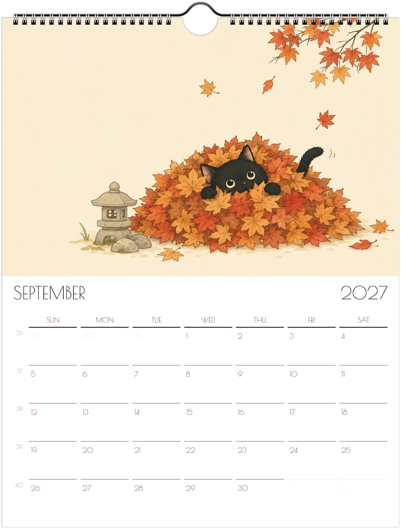 Puede incluir: Un calendario de pared para septiembre de 2027 con una ilustraci&oacute;n de un gato negro asom&aacute;ndose desde un gran mont&oacute;n de hojas de arce oto&ntilde;ales naranjas y rojas, con una peque&ntilde;a linterna de piedra cerca y hojas cayendo sobre un fondo crema.