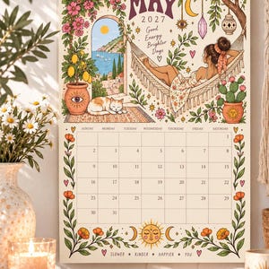 May include: A wall calendar for May 2027 featuring a colorful illustration of a person resting in a hammock, a sleeping cat, a lemon tree, and a coastal view. The calendar grid includes dates from the 1st to the 31st, decorated with floral borders and celestial sun and moon motifs.