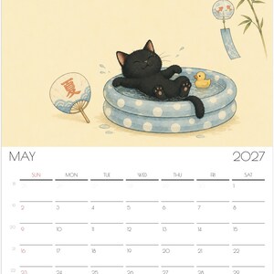 Puede incluir: Una p&aacute;gina de calendario de pared para mayo de 2027 con la ilustraci&oacute;n de un gato negro relaj&aacute;ndose en una piscina inflable azul con lunares blancos junto a un patito de goma amarillo, un abanico redondo con el car&aacute;cter japon&eacute;s de verano y un carill&oacute;n.