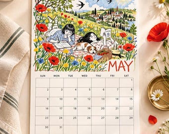 May include: A wall calendar for May 2027 featuring an illustration of two people and a dog resting in a field of red poppies and wildflowers. The scene includes a picnic basket, a distant village, and birds in a blue sky. The calendar grid is below.