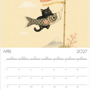 Puede incluir: Un calendario de pared para abril de 2027 con una ilustraci&oacute;n de un gato negro aferrado a una manga de viento de pez koi gris sujeta a un poste de bamb&uacute;. El fondo muestra un cielo amarillo p&aacute;lido, una monta&ntilde;a lejana y ramas de cerezo.