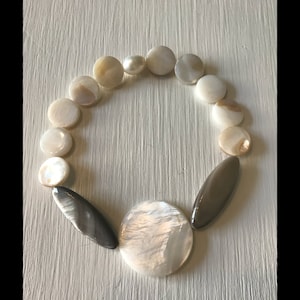 May include: A white and brown shell bracelet with a large, round, white shell pendant.