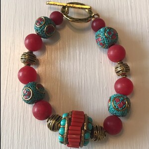 May include: A red and turquoise beaded bracelet with a gold clasp and a large, red and turquoise bead in the center.