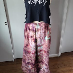 May include: A black cropped tank top with the text "GOOD VIBES" printed in white. The tank top is paired with wide-leg pants with a tie-dye pattern in shades of pink, purple, and green.