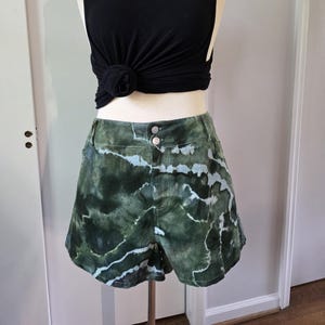 May include: Green and white tie-dye denim shorts with a black tank top and a silver necklace.