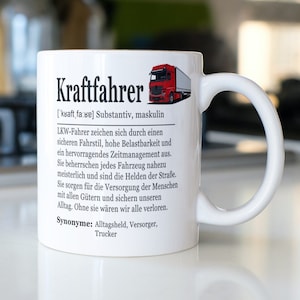 May include: A white ceramic mug with a black and white illustration of a semi-truck and the word "Kraftfahrer" in black text. The text below the illustration defines the word "Kraftfahrer" as a German noun for a truck driver. The text also includes synonyms for the word, such as "Alltagsheld", "Versorger", and "Trucker".
