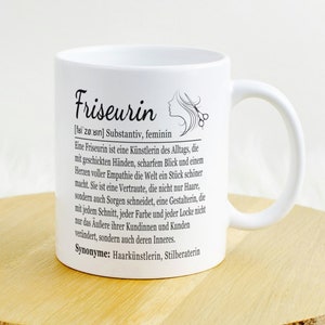 Op de afbeelding: Witte keramische mok met een zwart-wit ontwerp met de tekst "Friseurin [faizan] Substantiv, feminin" en een definitie van het woord. De mok heeft een zwart handvat.
