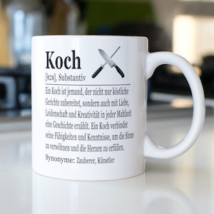 Op de afbeelding: Witte keramische mok met een zwart-wit ontwerp dat het woord "Koch" definieert als een zelfstandig naamwoord in het Duits. Het ontwerp bevat een definitie van het woord en twee gekruiste keukemessen.
