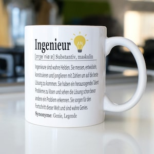 Pode incluir: Caneca de cerâmica branca com um design preto e amarelo. A caneca apresenta a palavra "Ingenieur" em texto preto com uma definição em alemão abaixo. A definição inclui as palavras "Helden" e "Genies".