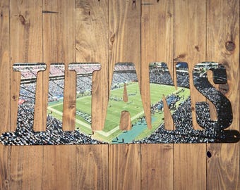 May include: A wooden sign with the word "TITANS" cut out, revealing a photo of a football stadium with a green field and a crowd of people.