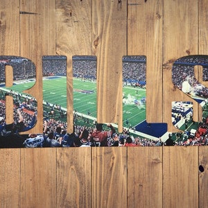 May include: A wooden sign with the word "BILLS" spelled out in large letters. The letters are filled with a photo of a football stadium with fans in the stands.