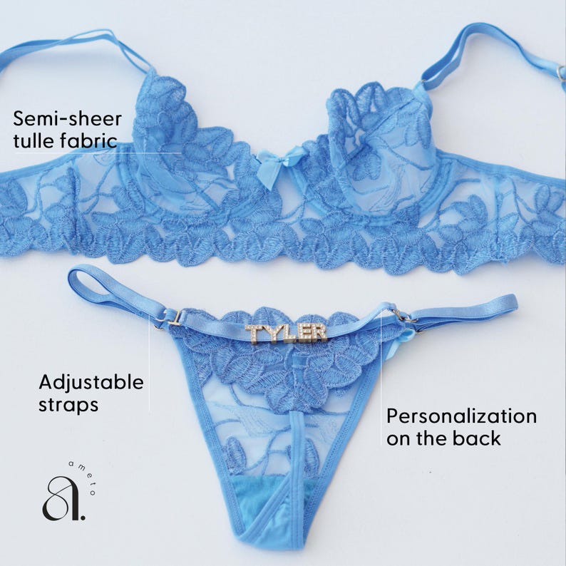 May include: Light blue lingerie set featuring a semi-sheer tulle fabric. The set includes a bra and a thong with adjustable straps. The thong has the name "TYLER" on the front. The bra has a bow in the center. The lingerie is designed with floral lace details.