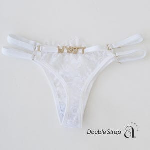 May include: White lace thong with double straps and gold-tone hardware. The word "WYATT" is spelled out in gold-colored rhinestones across the front. The thong features a delicate floral lace pattern.