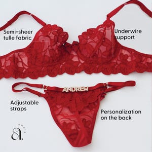 May include: A red lingerie set featuring a semi-sheer tulle bra with underwire support and a matching thong. The thong has adjustable straps and the name "ANDREW" on the front. The set is designed with floral lace details.