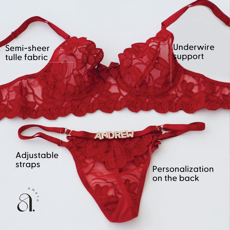 May include: A red lingerie set featuring a semi-sheer tulle bra with underwire support and a matching thong. The thong has adjustable straps and the name "ANDREW" on the front. The set is designed with floral lace details.