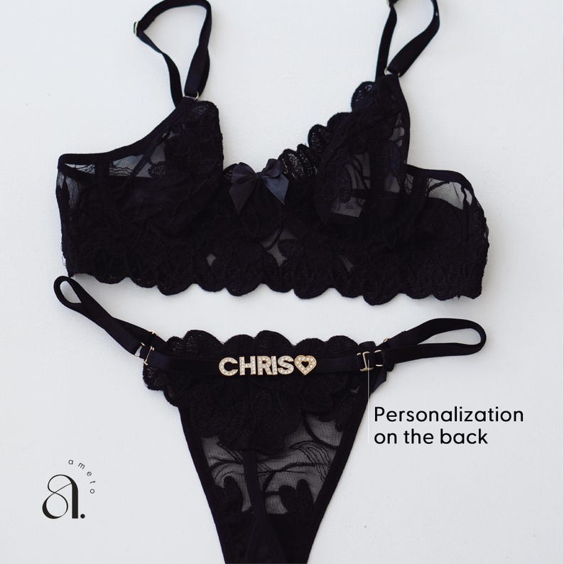 May include: Black lace lingerie set featuring a bralette and thong. The bralette has adjustable straps and a bow detail. The thong has the name "CHRIS" spelled out in rhinestones with a heart symbol. The set is displayed on a white background.