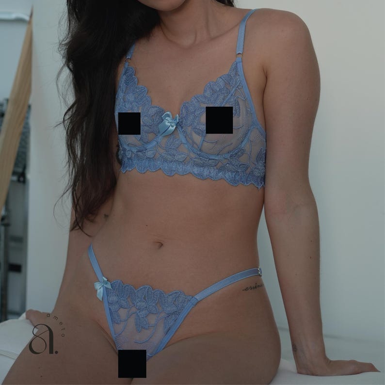 May include: Light blue lingerie set featuring a lacy bra with adjustable straps and a matching thong. The bra has a delicate floral pattern and a small bow in the center. The thong also has a floral design and a small bow. The set is made of a sheer, lightweight fabric.