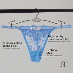 May include: Light blue G-string style underwear with floral embroidery and the name "TYLER" in rhinestones. The semi-sheer tulle underwear is hanging on a silver hanger.