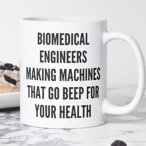 May include: White ceramic mug with black text that reads "Biomedical Engineers Making Machines That Go Beep For Your Health".