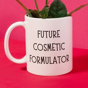 May include: White ceramic mug with a black inscription that reads "Future Cosmetic Formulator" and pink roses in the mug.