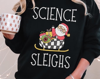 May include: Black sweatshirt with the text "SCIENCE SLEIGHS" in white. The graphic features Santa Claus in a sleigh with gifts. The sweatshirt is a crew neck style.