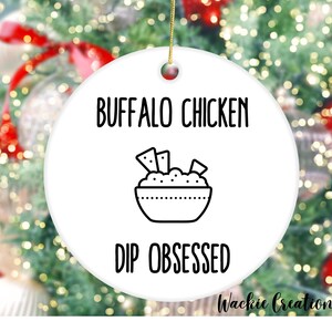 May include: White ceramic Christmas ornament with black text that reads "Buffalo Chicken Dip Obsessed" and a black line drawing of a bowl of dip with chips.