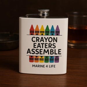 May include: A white stainless steel flask with a silver cap. The flask features a colorful crayon design above and below the text "CRAYON EATERS ASSEMBLE" and "MARINE 4 LIFE".