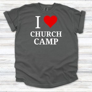 Puede incluir: Una camiseta gris oscuro con un gr&aacute;fico blanco que dice "Me encanta el campamento de la iglesia" con un coraz&oacute;n rojo.