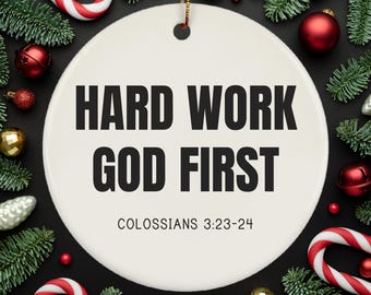 May include: White round Christmas ornament with the text "HARD WORK GOD FIRST" and the scripture reference "COLOSSIANS 3:23-24". The ornament is surrounded by green pine branches, red and gold ornaments, and candy canes.