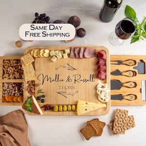 May include: A wooden serving board with a built-in drawer for cheese knives and a separate drawer for snacks. The board is personalized with the names "Mollie & Russell" and the date "7.14.2024".