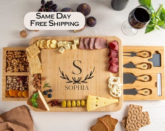 May include: A bamboo cheese board with a sliding drawer for snacks. The board has a personalized monogram with the letter "S" and the name "Sophia". It comes with four cheese knives and a small slate serving tray.