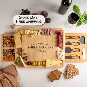 May include: A bamboo cheese board with a personalized engraving, surrounded by crackers, cheese, meats, nuts, and fruit. Includes a set of cheese knives and a bottle of wine. The board is engraved with "AMBER & EUGENE EST 2025".